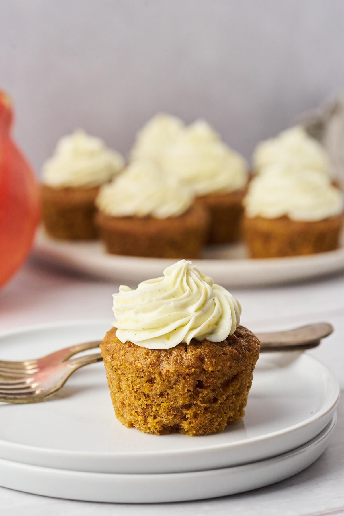 Pumpkin cupcake with cream cheese frosting on a plate with a platter in the background