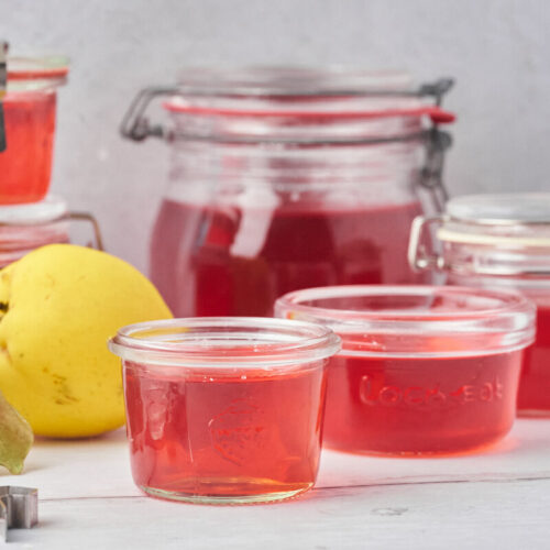 Red quince jelly in a jar with fresh quinces beside it