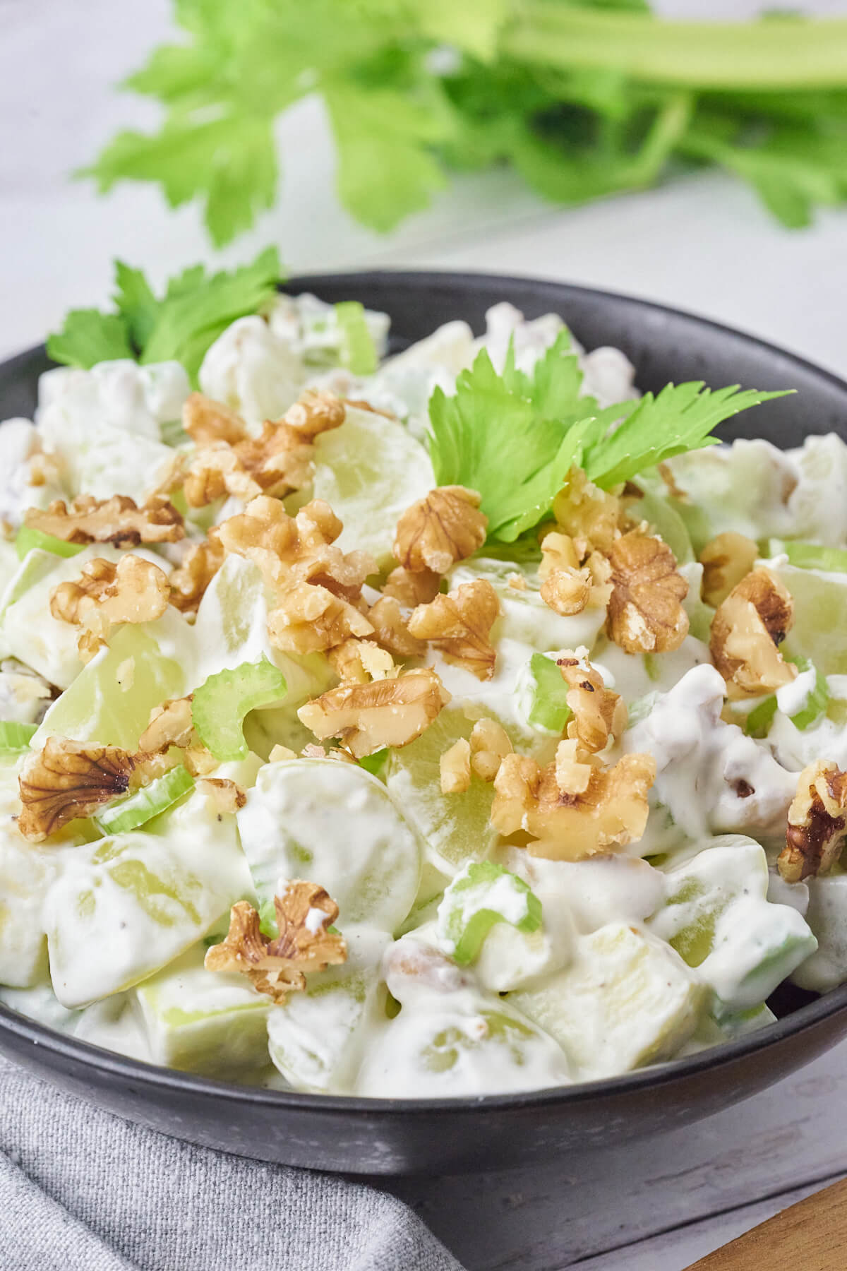 Serving of classic Waldorf salad garnished with celery leaves and chopped walnut kernels.