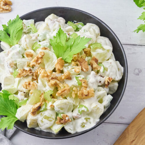 Old-fashioned Danish Waldorf salad with celery, apple, grapes, and walnuts served in a bowl and garnished with walnuts and celery leaves.