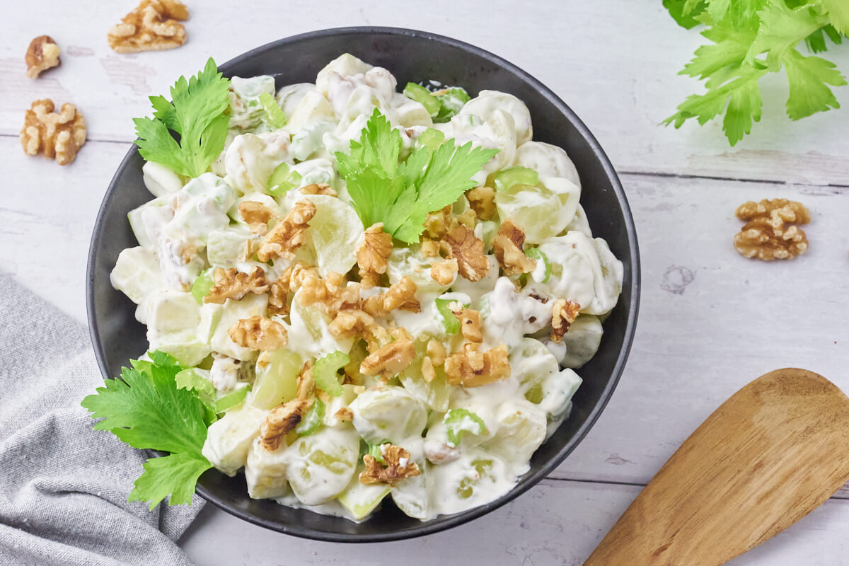 Old-fashioned Danish Waldorf salad with celery, apple, grapes, and walnuts served in a bowl and garnished with walnuts and celery leaves.